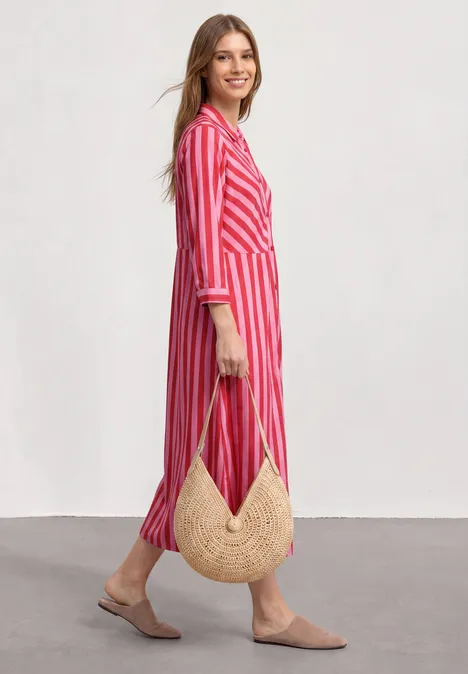 Femme en robe chemise longue à rayures roses et blanches, sac en paille rond et mules beiges