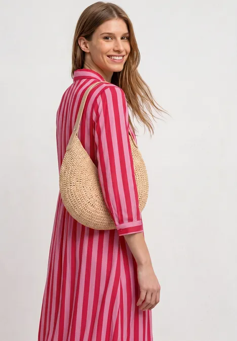 Femme de dos en robe midi rose et rouge à rayures, manches 3/4, portant un sac rond en paille sur l’épaule