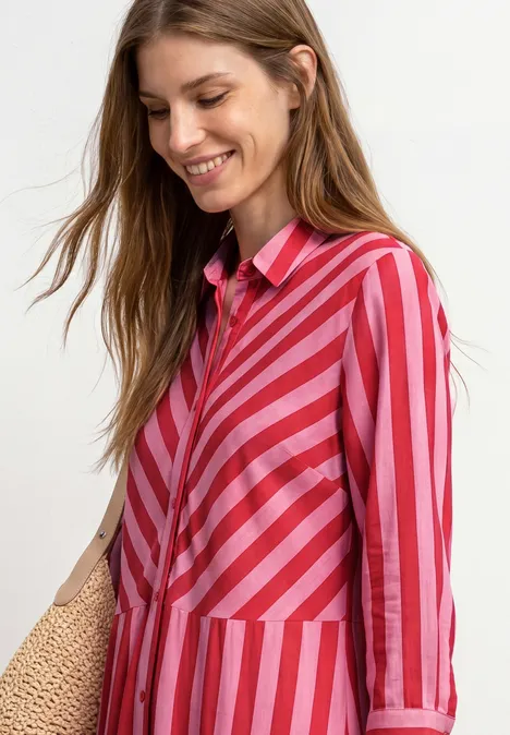 Une femme en chemise rayée rouge et rose tient un sac en paille.