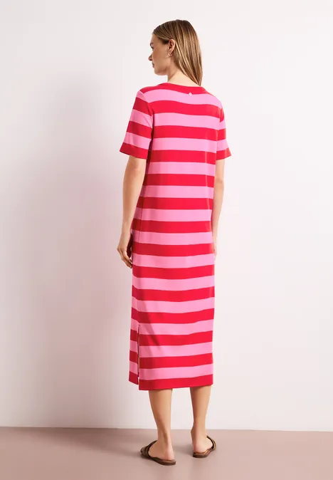 Eine Frau steht seitlich im gestreiften Midi-Kleid in Rot- und Pinktönen.