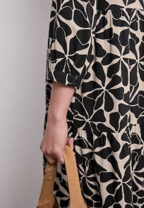 Person in schwarz-weiß gemustertem Kleid hält eine braune Handtasche.