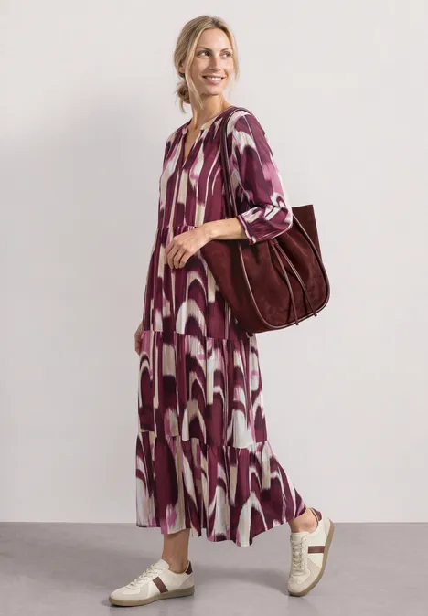 Midi-Kleid mit Split Neck im Ethno-Look rustic rouge Frau in violett-weiß gemustertem Midi-Kleid mit Turnschuhen und großer brauner Tasche, schlendert elegant.