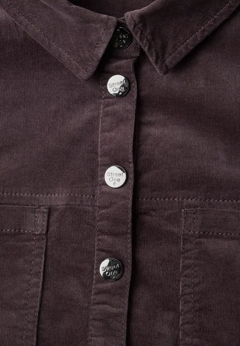 Nahaufnahme einer dunkelbraunen Cordjacke mit silbernen Metallknöpfen und Brusttaschen.