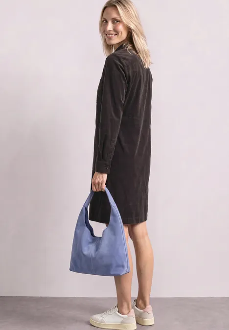 Femme en robe noire et baskets blanches, tenant un sac bleu et regardant en souriant par-dessus l'épaule.