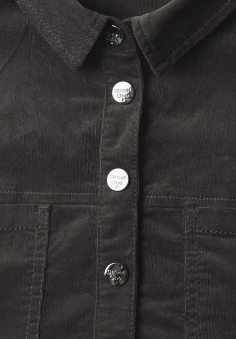 Gros plan d'une veste en velours côtelé marron foncé avec col et pressions argentées.