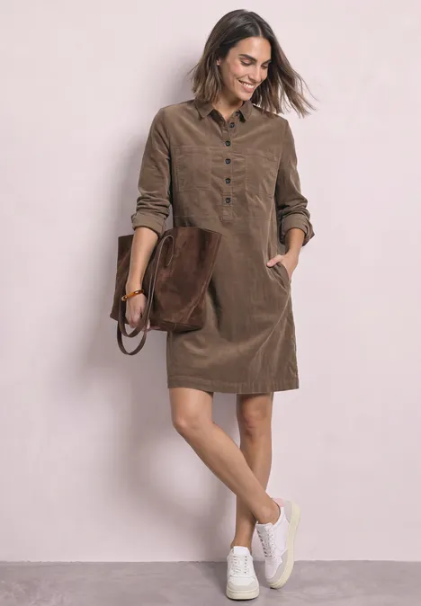 Knielanges Kleid aus softem Cord velvet mocha Frau trägt braunes Cordkleid mit Eingrifftaschen, weiße Sneaker und Schultertasche.