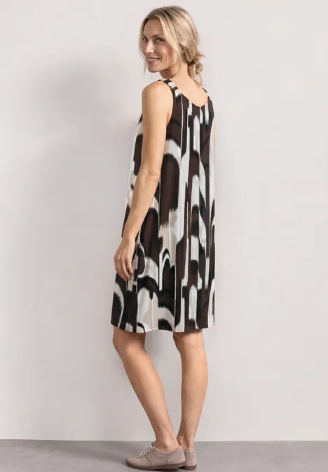 Robe mi-longue à bretelles froncées espresso brown Frau in lockerem, ärmellosem Kleid mit abstraktem Schwarz-Weiß-Muster, Seitenansicht vor hellem Hintergrund.