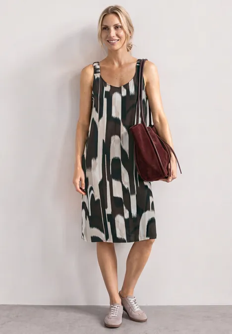 Robe mi-longue à bretelles froncées espresso brown Frau trägt ärmelloses, schwarz-weiß gemustertes Midikleid und hält eine rote Umhängetasche.