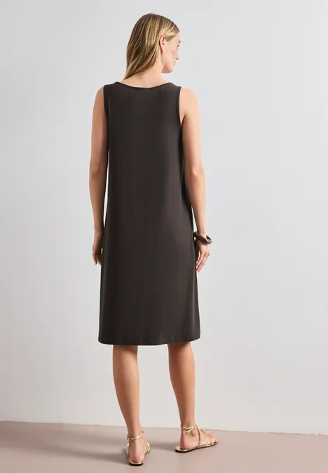 Frau von hinten in einem schlichten, ärmellosen knielangen schwarzen Kleid und flachen Sandalen.