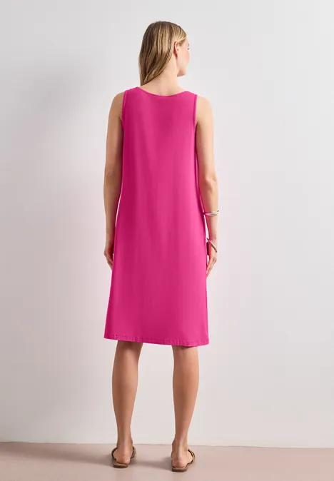 Person im pinken ärmellosen Kleid und Sandalen, Rückenansicht.
