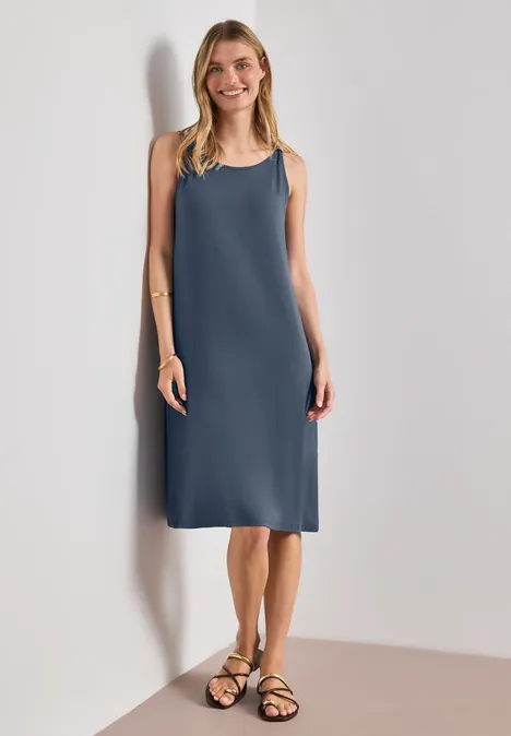Knielanges Kleid mit Schnallendetail ashen blue Frau in ärmellosem knielangem blauem Kleid und schwarzen Sandalen vor hellem Hintergrund.
