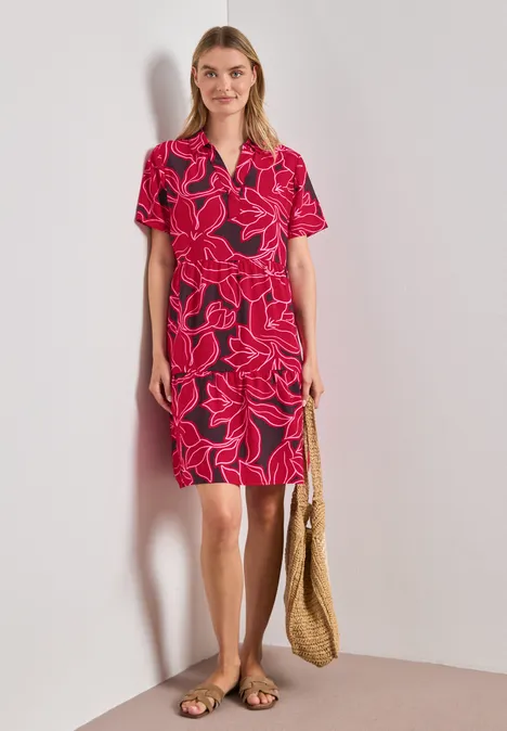 Frau in rotem Blumenkleid mit V-Ausschnitt, kurzen Ärmeln, Strohtasche und flachen Sandalen