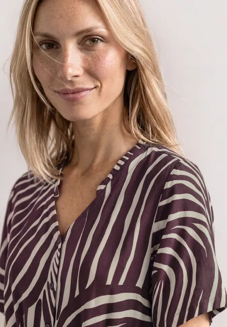 Frau mit blonden Haaren trägt lila-weiße Bluse mit Zebramuster und V-Ausschnitt.