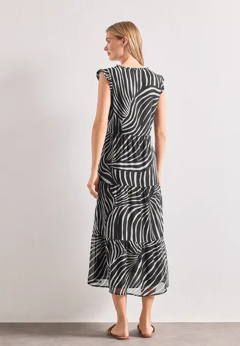 Femme en robe midi à motif zèbre noir et blanc, de dos, légèrement de profil, sur fond clair.