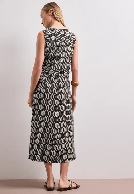 Rückenansicht einer Frau in ärmellosem, midi-langem Kleid mit geometrischem Schwarz-Beige-Muster und Taillengürtel