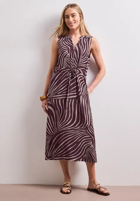 Frau trägt ärmelloses Midikleid mit Zebramuster, Wickeloptik und flachen Sandalen.