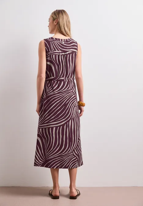 Frau von hinten in ärmellosem, midi-langen Kleid mit lila-weißen Zebramuster und flachen Sandalen.