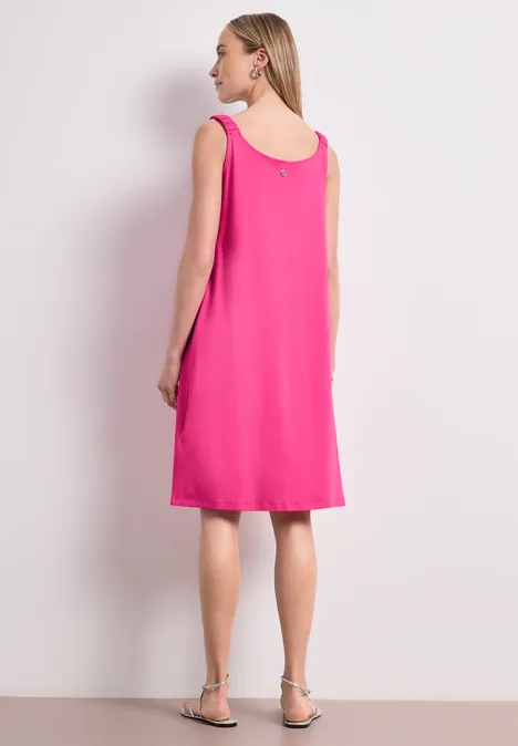 Frau in ärmellosem pinkfarbenem Kleid, Rückenansicht, mit flachen Sandalen.