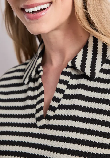Femme souriante porte un polo rayé noir et blanc, col apparent.