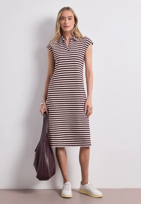 Femme en robe midi à rayures et col polo, baskets blanches et grand sac sur fond neutre.