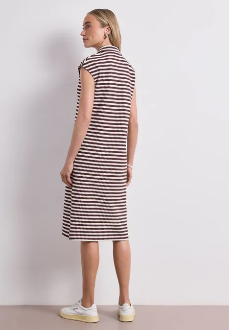 Femme en robe rayée jusqu'aux genoux et baskets blanches sur fond gris clair.