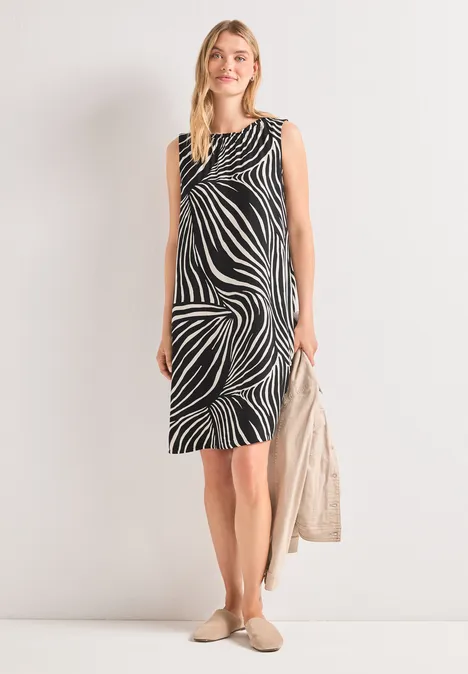 Frau in ärmellosem, knielangem Kleid mit schwarz-weißem Zebramuster, hält eine helle Tasche.