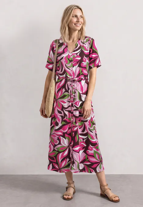 Midi-Kleid mit V-Neck und Print magenta dream Frau in knöchellangem, kurzärmeligem Kleid mit rosa-grünem Blattmuster, Sandalen und Strohtasche.