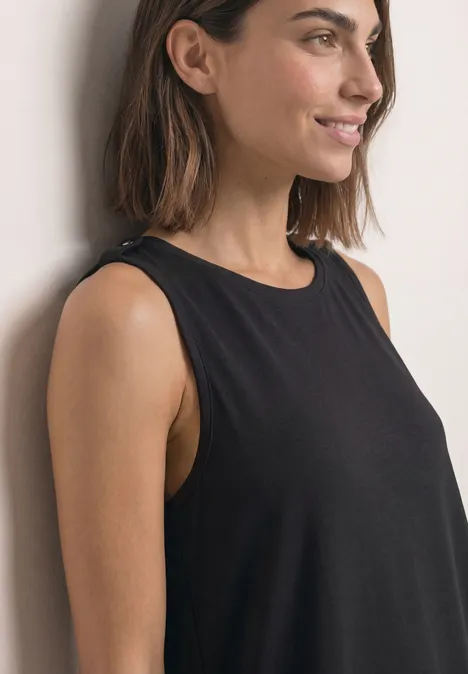 Eine Frau mit schulterlangem braunem Haar in einem schwarzen ärmellosen Top lächelt seitlich.