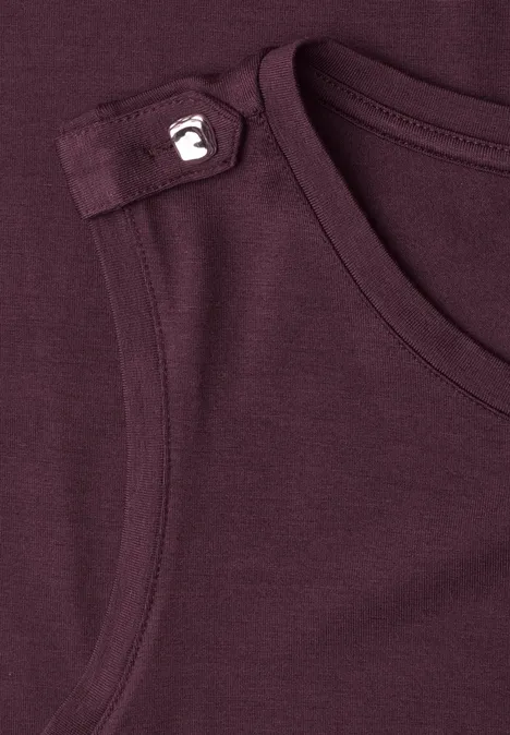 Close-up van een donker wijnrode tanktop met een klein wit apenlogo op de schouder.