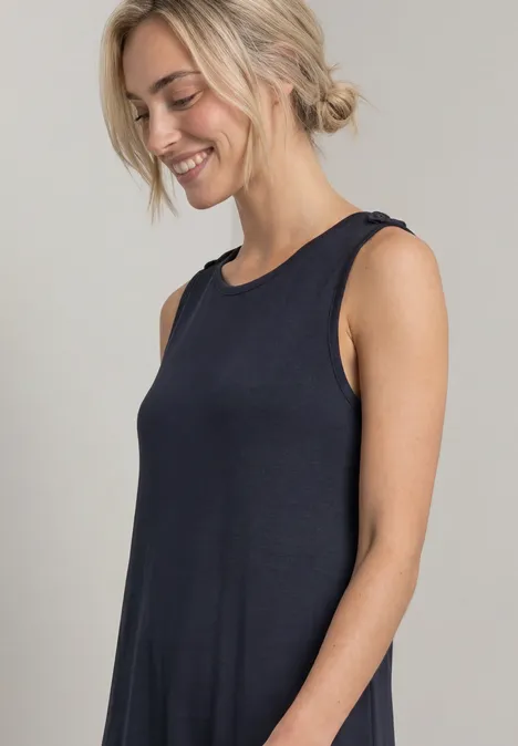 Blonde vrouw in een donkerblauw mouwloos topje, glimlacht en kijkt naar beneden.