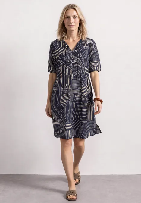 Eine Frau trägt ein blau-weiß gemustertes, knielanges Kleid mit V-Ausschnitt, kurzen Ärmeln und Sandalen.