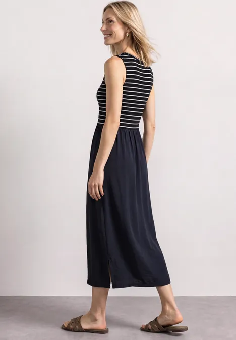 Frau in gestreiftem ärmellosem Oberteil, weitem Culotte-Style-Rock und braunen Sandalen, seitlich stehend.