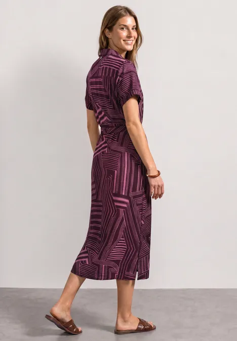 Frau in violettem, gemustertem Midikleid und flachen Sandalen.