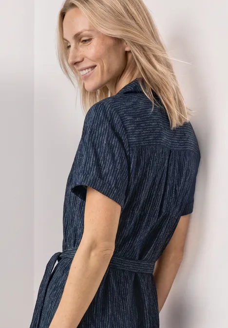 Femme aux cheveux blonds mi-longs porte une robe-chemise marine cintrée à manches courtes.