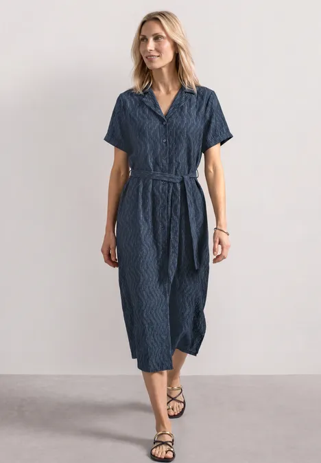 Frau in tailliertem, navyblauem Midikleid mit kurzen Ärmeln, V-Ausschnitt und Gürtel vor schlichtem Hintergrund