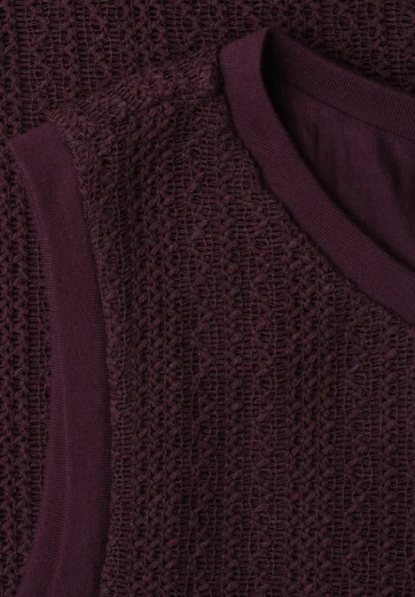 Close-up van een mouwloos, bordeauxrood gebreid topje met V-hals en gestructureerd patroon
