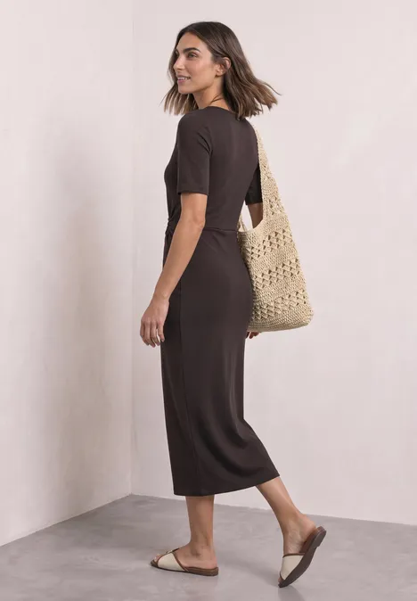 Midijurk van jersey met wikkel-look black coffee Vrouw in een bruine midi-jurk, draagt een gevlochten strooien tas en sandalen.