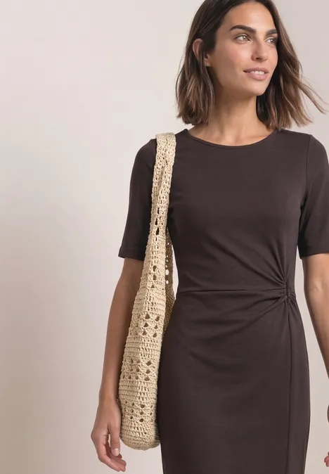 Midijurk van jersey met wikkel-look black coffee Vrouw in bruine, knielange jurk met zijtwist en korte mouwen draagt een gehaakte schoudertas.