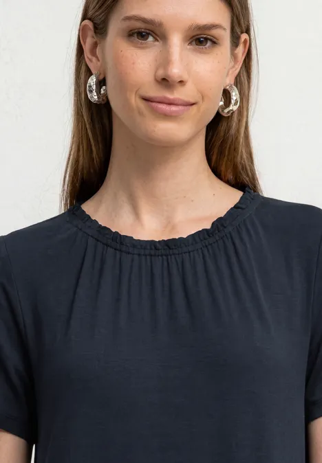 Eine Frau mit langen Haaren trägt ein schwarzes T-Shirt und silberne Ohrringe.