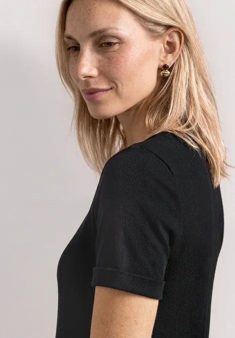 Midikleid in Rippstruktur mit Rundhals Black Blonde Frau schaut seitlich zur Kamera, trägt schwarzes Kurzarmshirt und goldene Ohrringe.