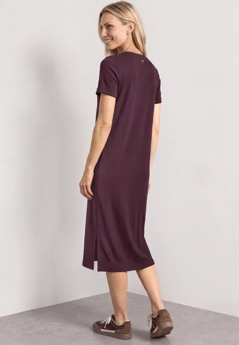 Vrouw van achteren in een loszittende, bordeauxrode midi-jurk met korte mouwen en platte schoenen.