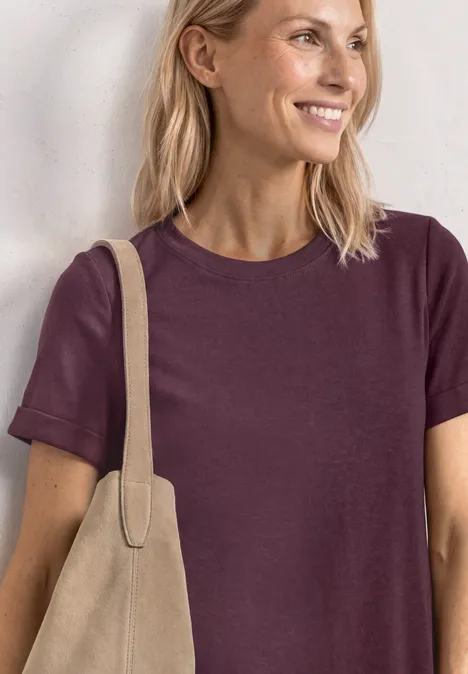 Vrouw met blond haar draagt een paarse t-shirt en een beige tas.