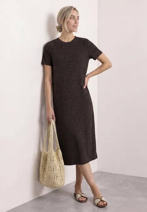 Frau trägt schwarzes T-Shirt-Kleid mit kleinen Punkten, flache Sandalen und hält eine gehäkelte Tasche.