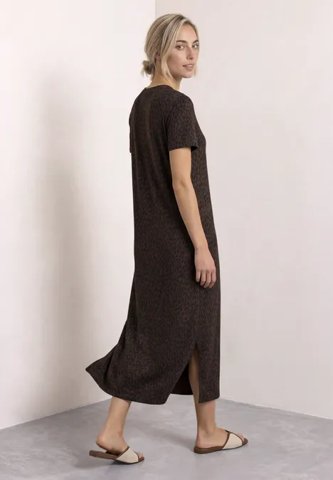 Frau im dunkelbraunen, kurzärmeligen Midikleid mit seitlichem Schlitz und Sandalen vor hellem Hintergrund.