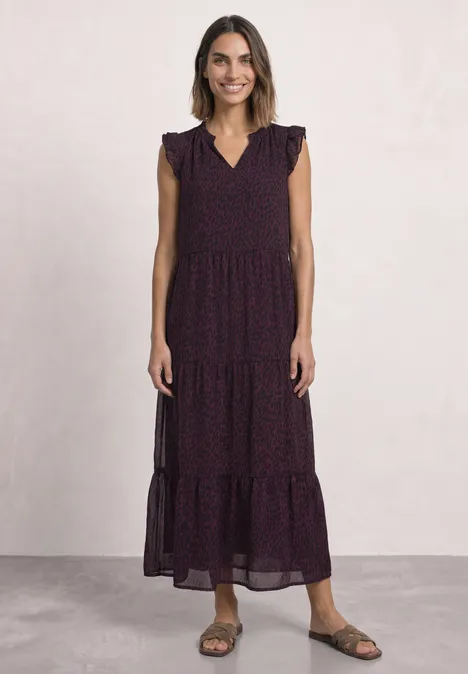 Femme portant une robe longue sans manches à étages avec volants et motif floral, sandales aux pieds.