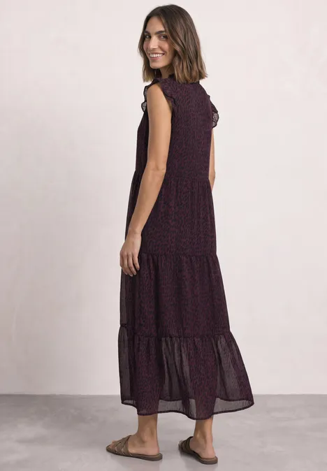 Femme souriant de profil portant une robe midi fluide sans manches, à volants et motif discret, avec sandales plates