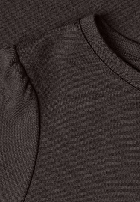 Close-up van de halslijn van een donkerbruin T-shirt met geplooid schouderdetail.