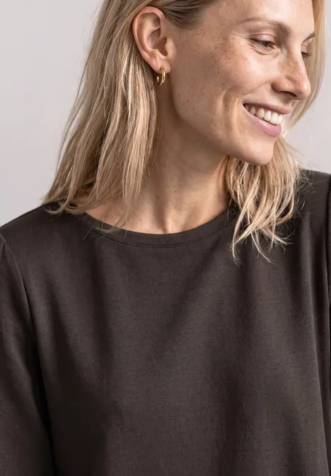 Portret van een glimlachende vrouw met blond haar, gouden oorbellen en een zwart shirt.