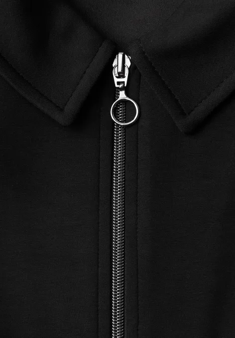 Nahaufnahme eines schwarzen Kleidungsstücks mit silbernem Reißverschluss und rundem Zipper-Anhänger.