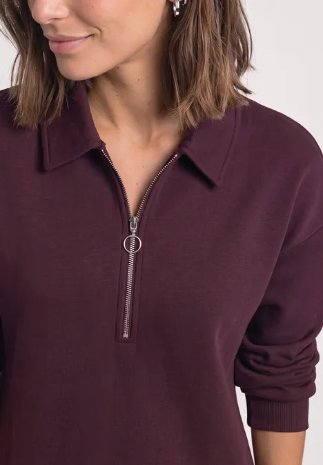 Femme portant un polo à manches longues violet foncé avec une demi-fermeture éclair ornée d’un anneau.